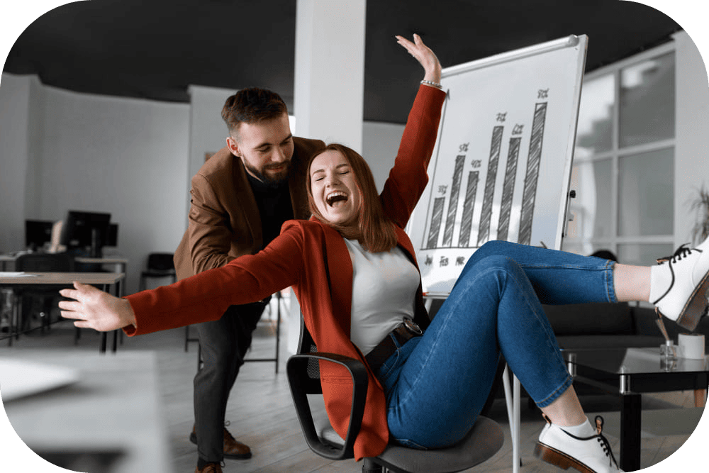 Two cheerful crypto SEO employees celebrating success in a bright office, laughing and high-fiving with computers and charts in the background.